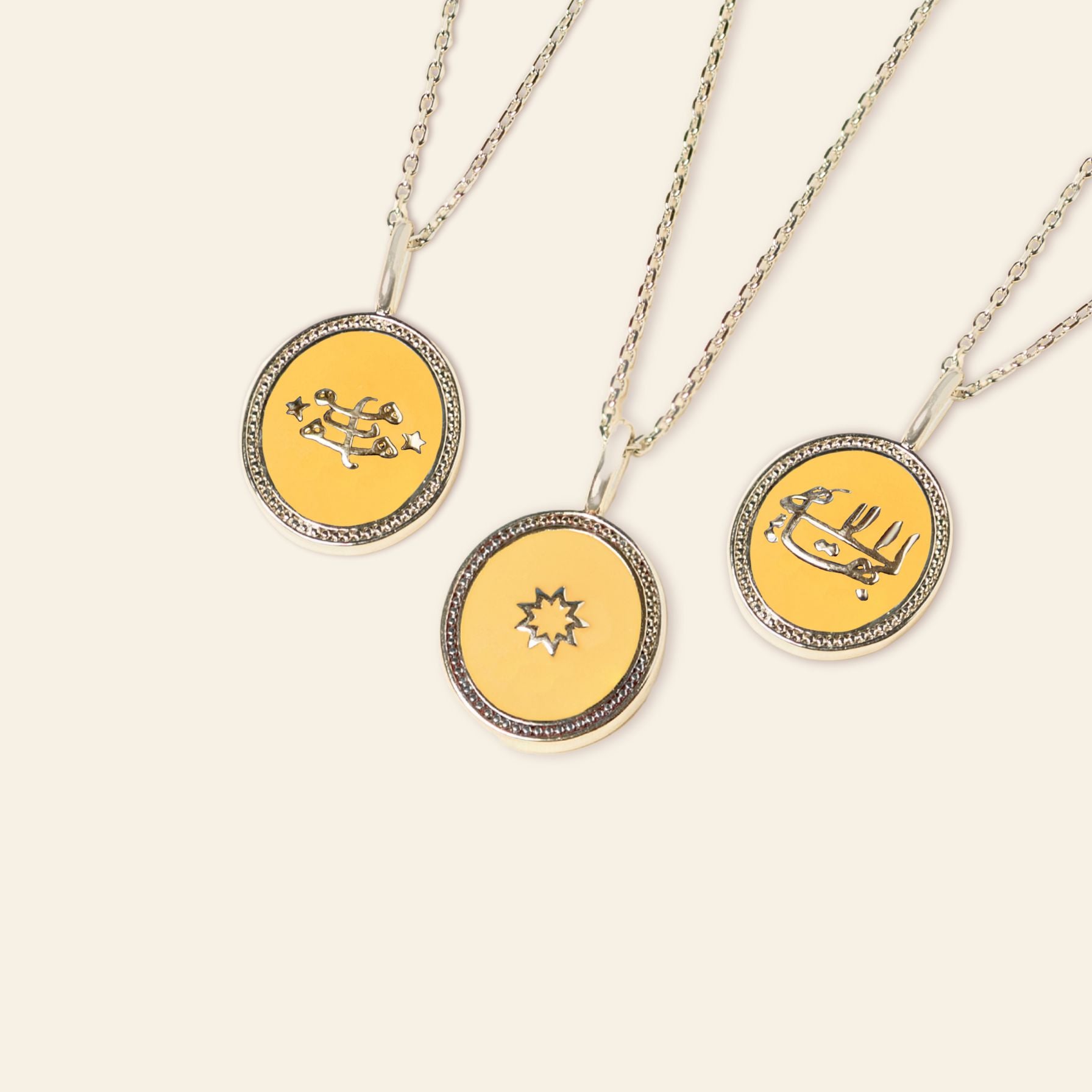 Three circular pendant necklaces with silver frames on a white background, each featuring a unique yellow and black enamel design incorporating the Ringstone Symbol.