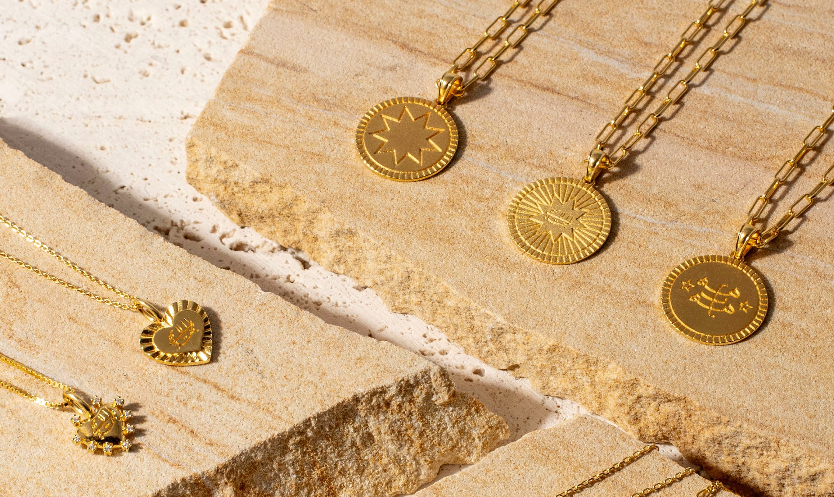 gold bahai pendant necklaces laid out on a textured stone surface