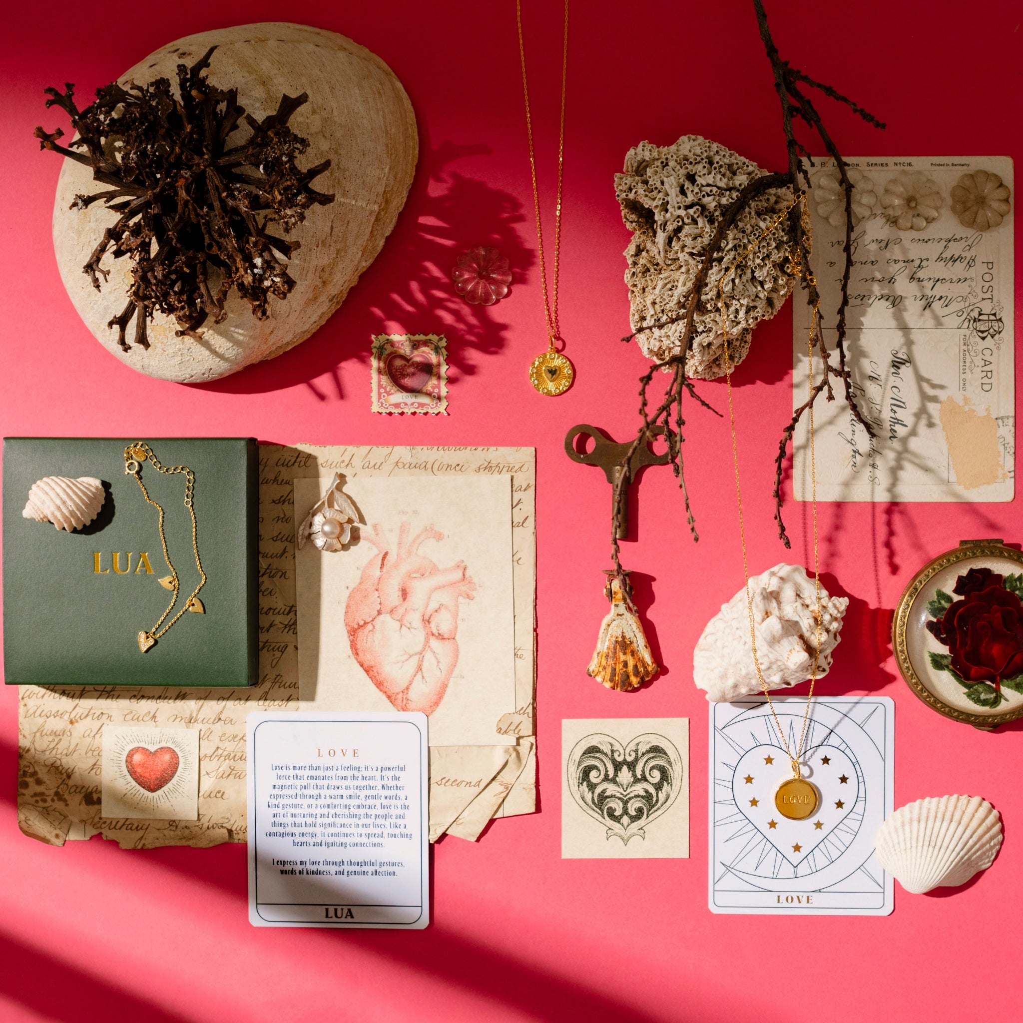 A flat lay of various items, including a love heart necklace, seashells, old letters, a key, and cards on a red background.