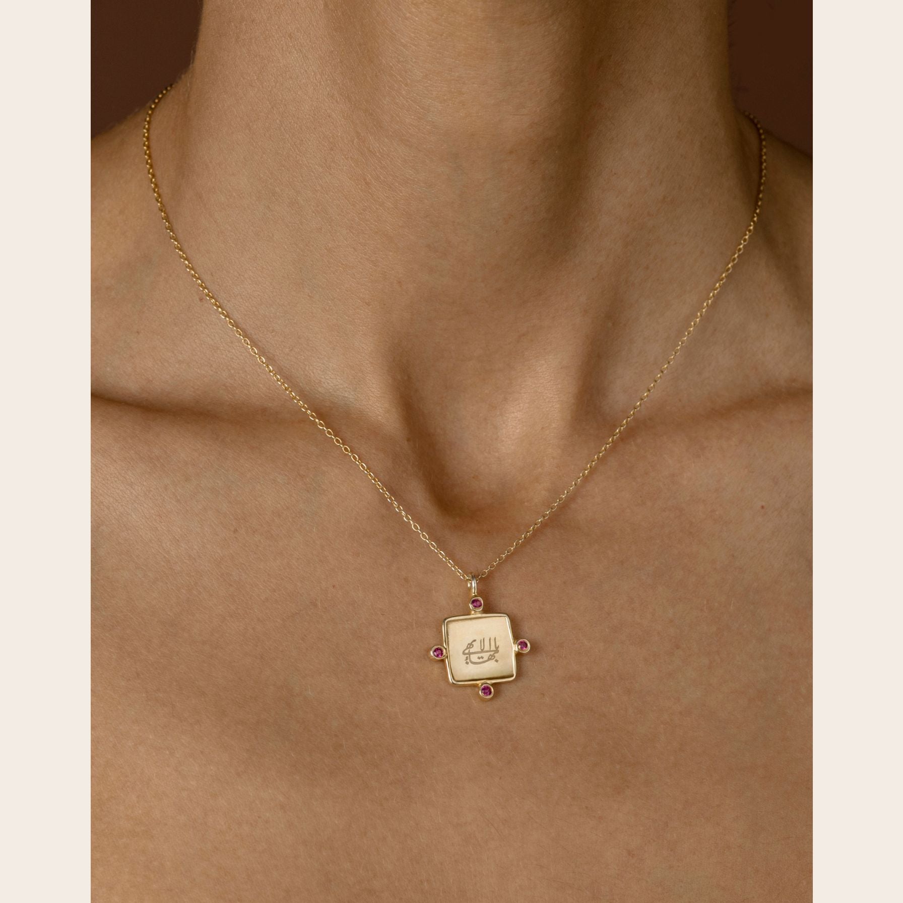 Gold necklace with a square greatest name pendant on a person's neck against a neutral background