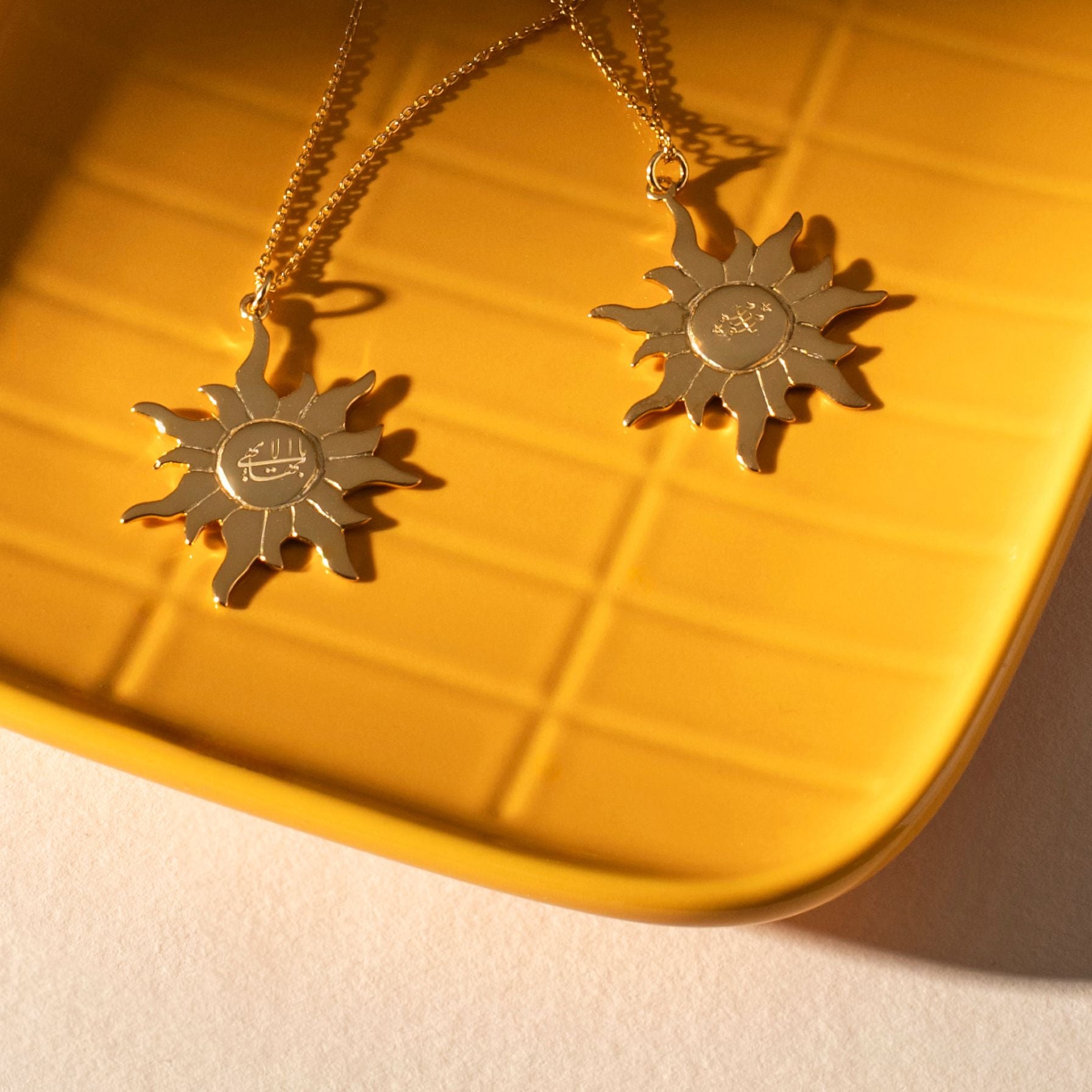Two gold sun-shaped pendants on a yellow surface