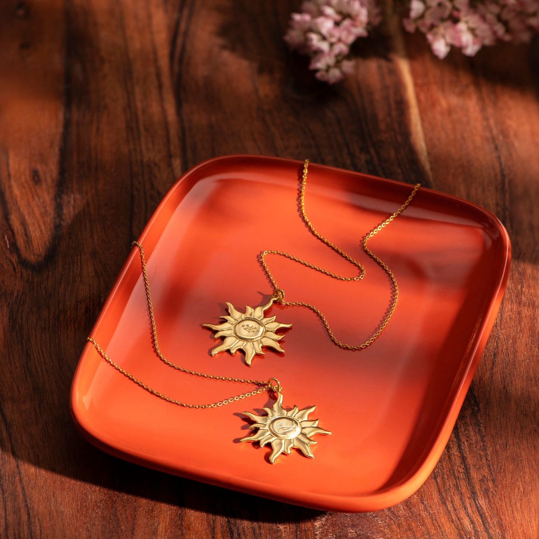 Gold necklace with sun-shaped ringstone, greatest name pendants on an orange tray against a wooden background