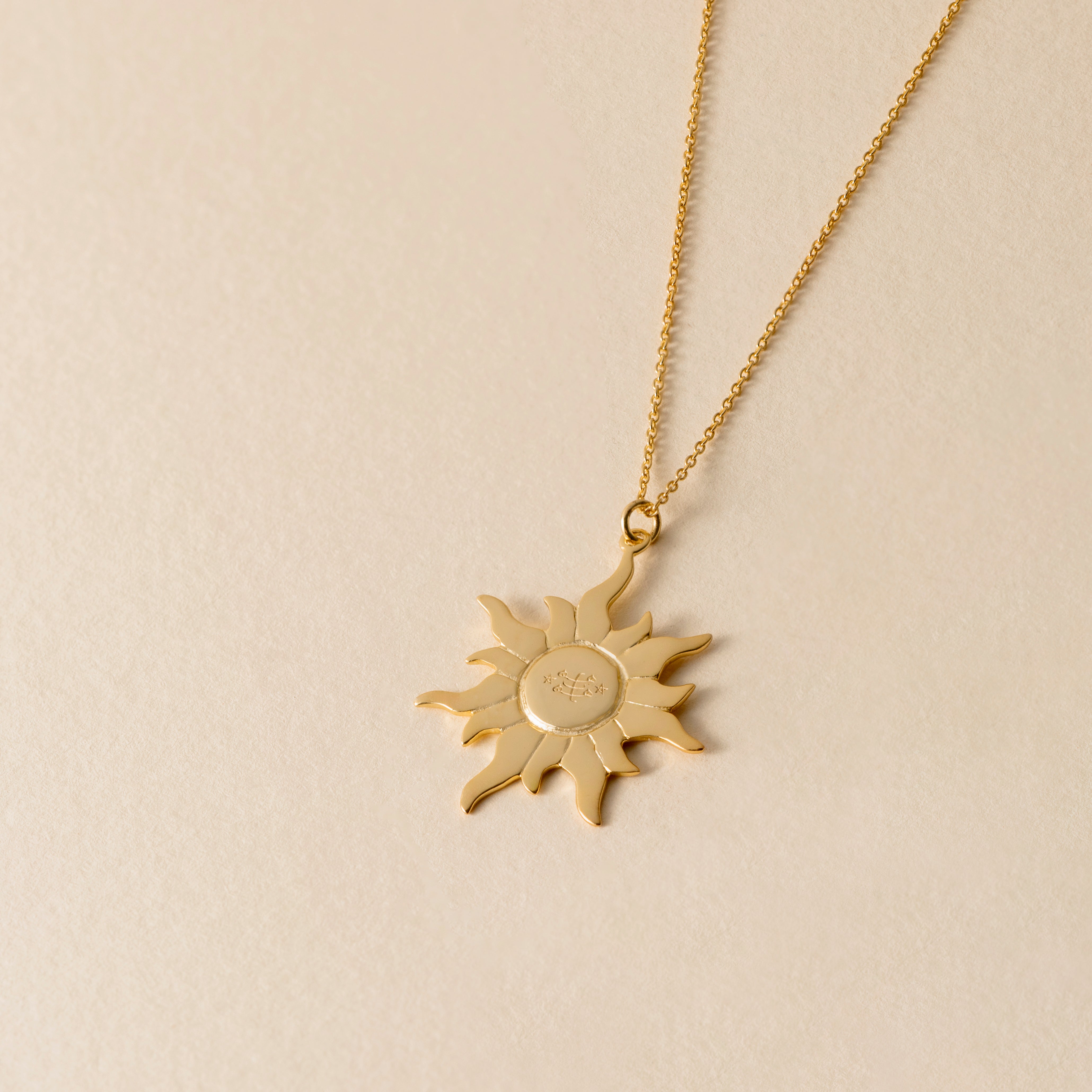 Gold sun-shaped pendant necklace on a beige background