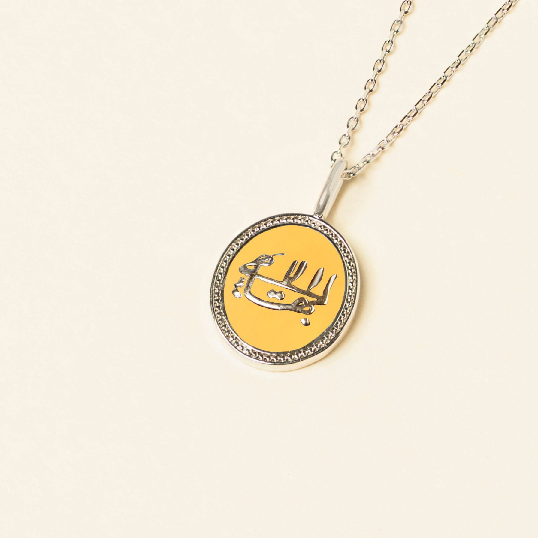 Silver necklace with a yellow pendant featuring the greatest name symbol, displayed on an enamel jewelry background.