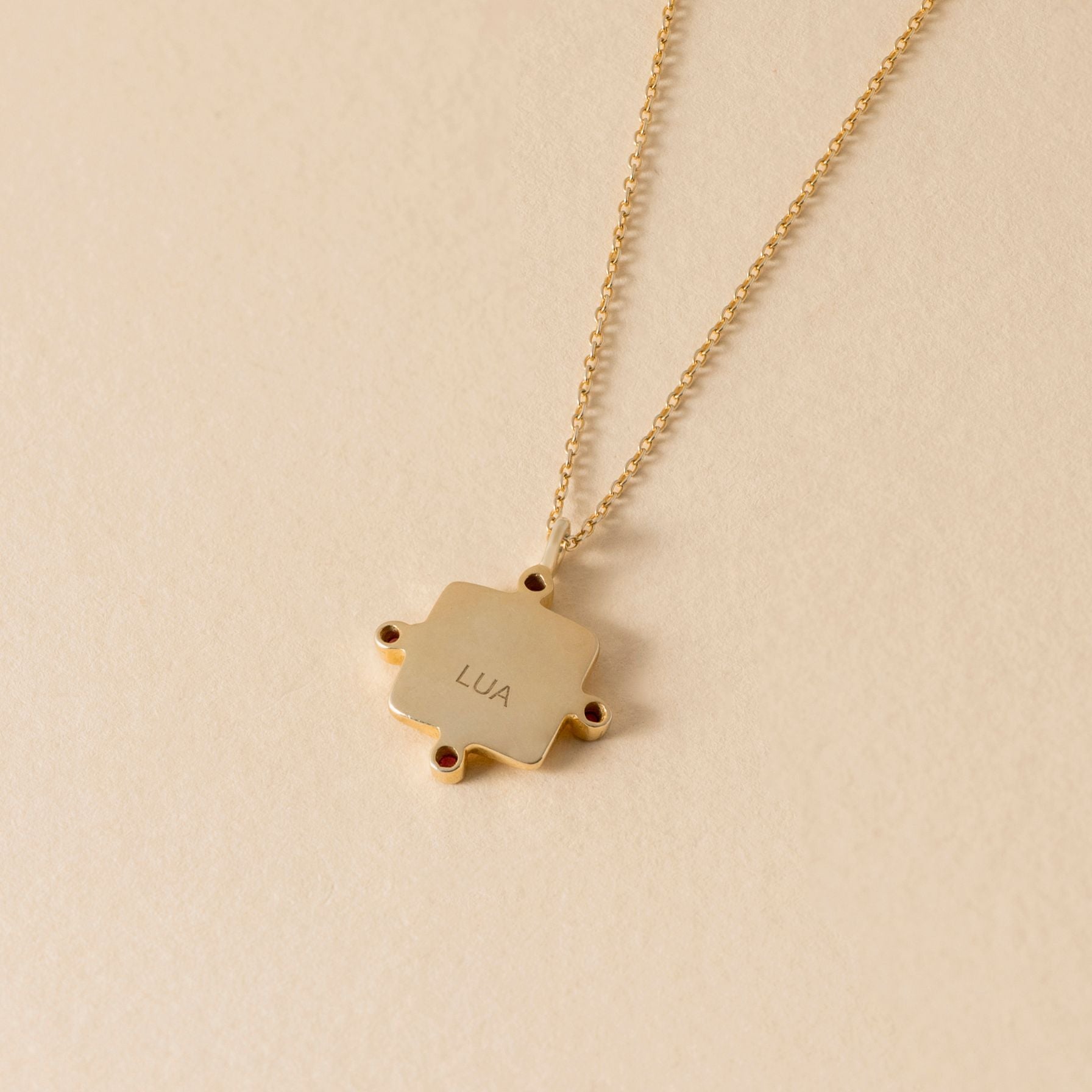 Gold lua necklace with a square pendant on a beige background