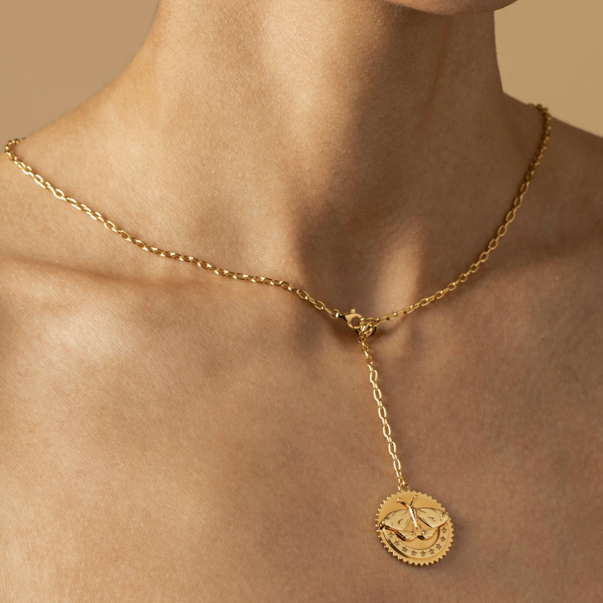 A gold butterfly necklace featuring a pendant with an intricate design is worn around a neck. The pendant, symbolizing transformation and resilience, is connected by a short chain, hanging slightly below the collarbones.