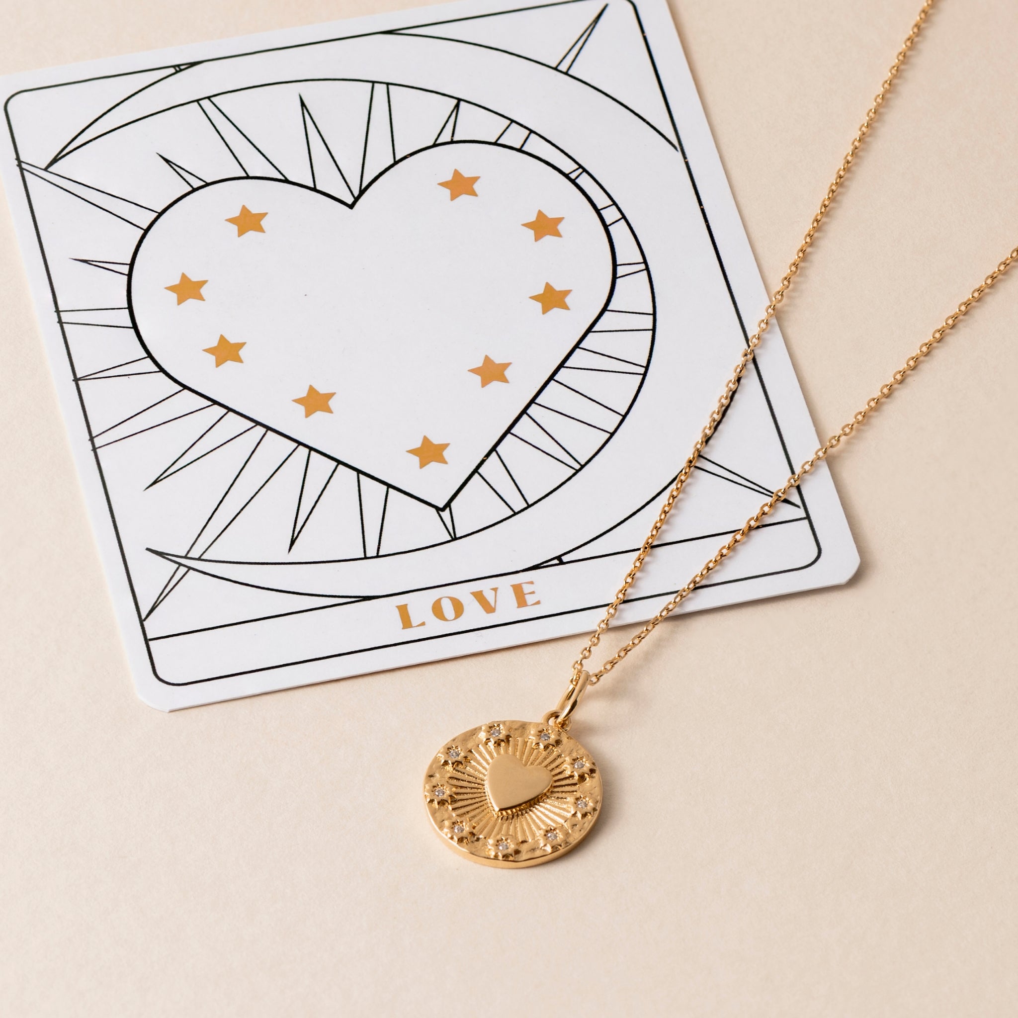 A Love Heart Necklace with a gold heart pendant is placed on a card adorned with a heart and star design, showcasing the word "LOVE" to capture affection's warmth.