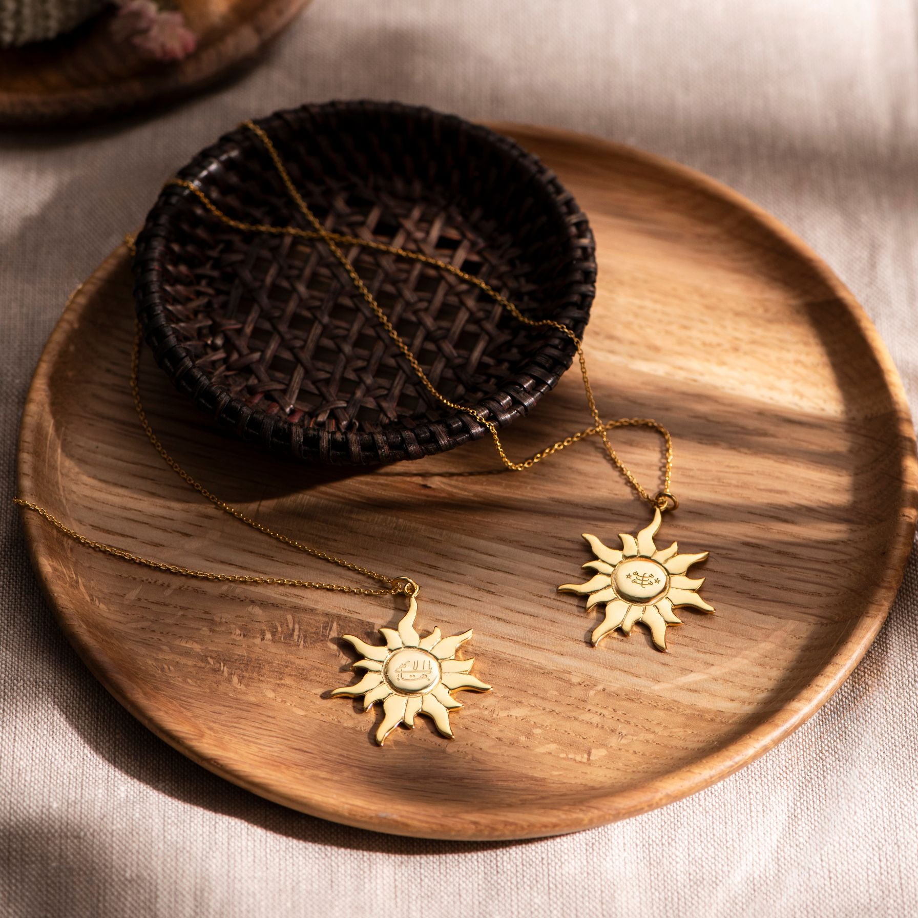 Gold sun-shaped greatest name ringstone neckalces on a wooden plate with a textured background