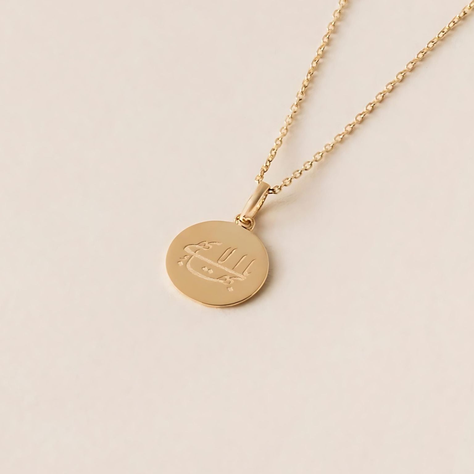 A gold necklace with a circular pendant engraved with a minimalist design, Ringstone Symbol the Splendour Halo, is elegantly placed on a light beige background.
