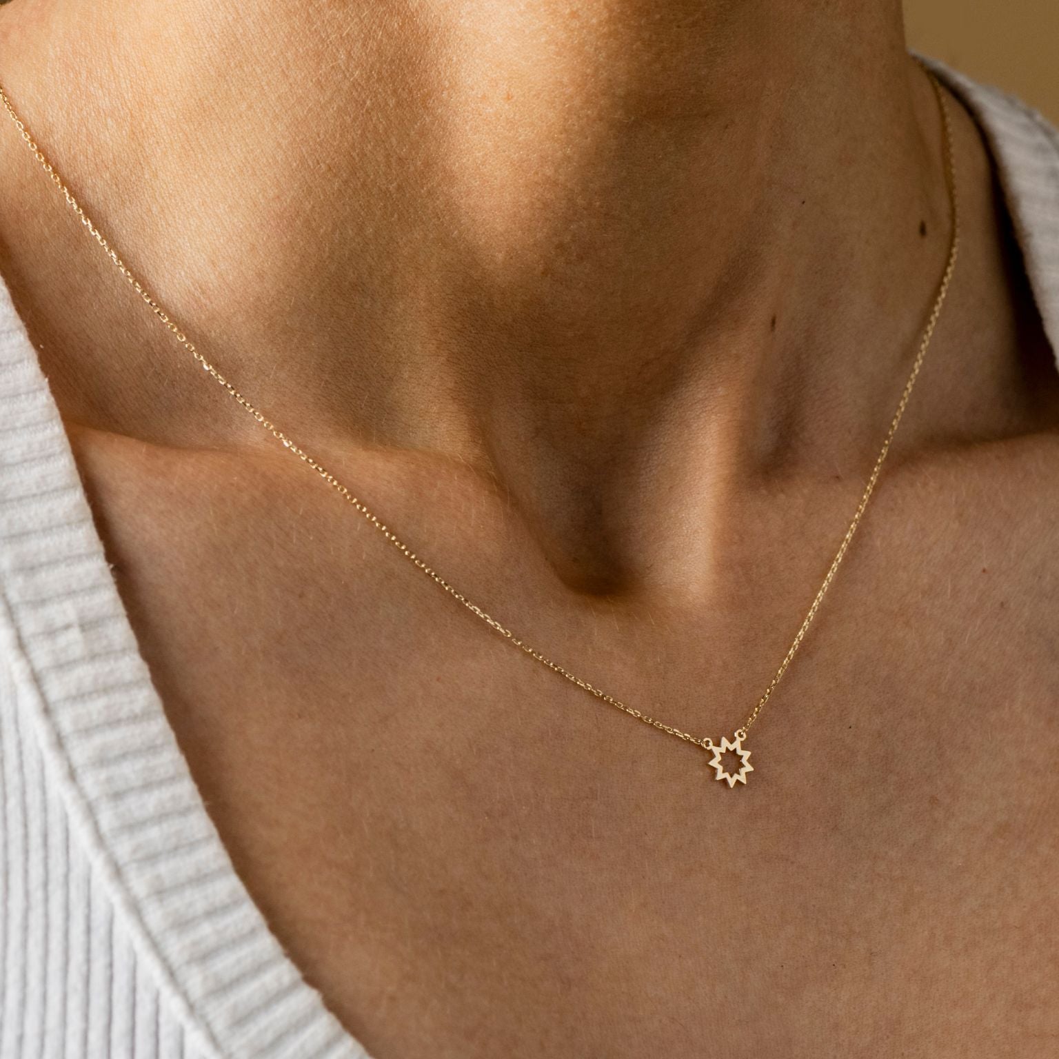 Close-up of a person's neck wearing the Brightest Star Necklace, featuring a delicate nine-pointed symbol pendant in gold, set against a light-colored, ribbed top.