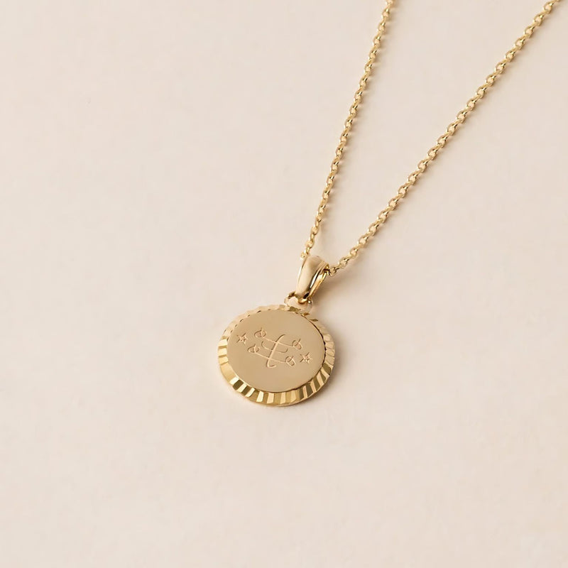 A gold necklace with a round pendant featuring an engraved Ringstone Symbol design .