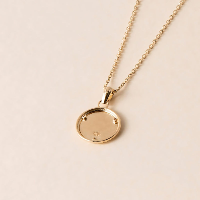 back view of a round gold pendant on a fine gold chain displayed on a cream background