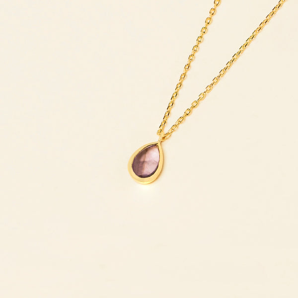 Gold Mona Necklace with a single teardrop-shaped Amethyst pendant on a light beige background.