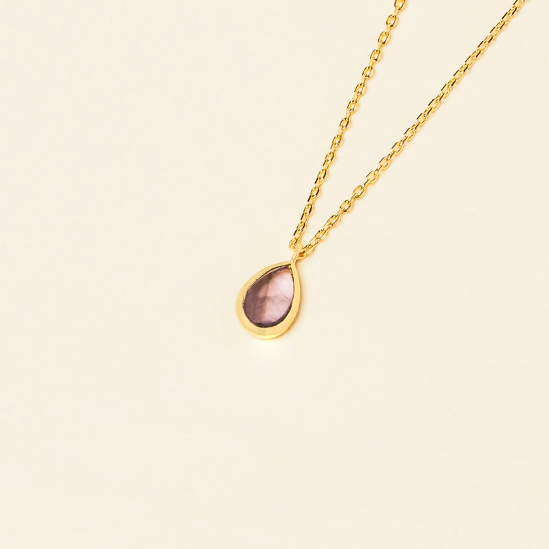 Gold Mona Necklace with a single teardrop-shaped Amethyst pendant on a light beige background.