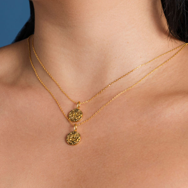 Close-up of a woman's neck wearing two layered gold necklaces with hammered disk pendant details against a neutral background.