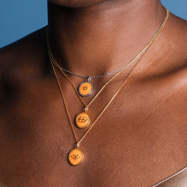 Close-up of a person's neck wearing three layered necklaces, two gold and one silver, each pendant featuring intricate designs including the Nine-Pointed Star.