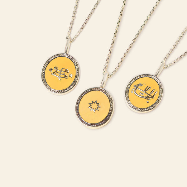 Three circular pendant necklaces with silver frames on a white background, each featuring a unique yellow and black enamel design incorporating the Ringstone Symbol.