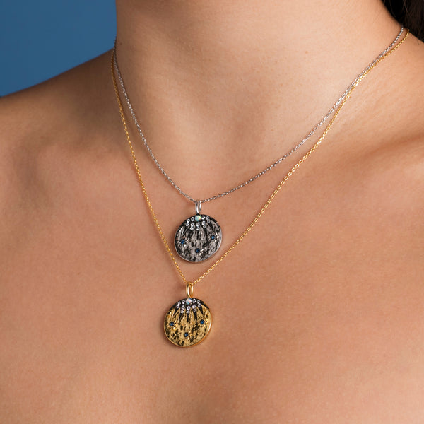 Close-up of a woman wearing two layered necklaces, one silver with a nine-pointed star pendant and one gold with an opal stone pendant.