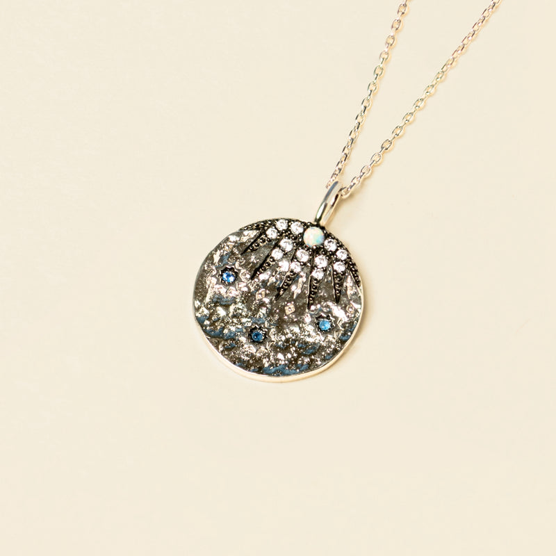 A circular pendant necklace with the nine pointed star embedded with sapphire blue cubic zirconia and clear crystals on a light background.