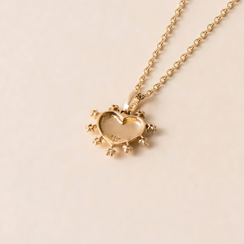 back view of a Gold heart-shaped pendant necklace with small cubic zirconia gemstones outlining the heart and featuring a subtle Greatest Name engraving, displayed on a light background.