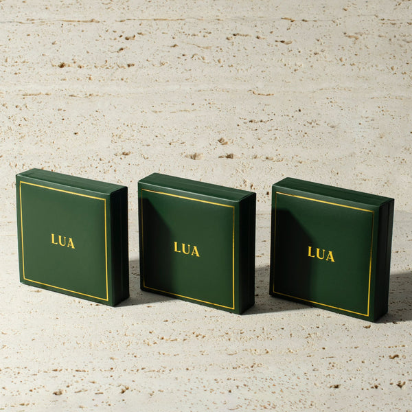 Three green boxes with yellow trim and the word "LUA" printed on them, arranged in a row on a beige textured surface, evoke a timeless style.