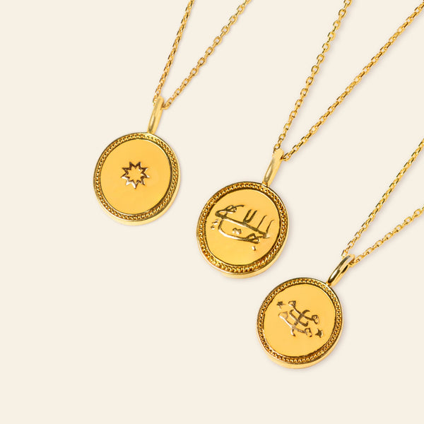 Three gold pendant necklaces on a pale background, each featuring different embossed designs: the greatest name, a nine-pointed star, and a ringstone symbol.