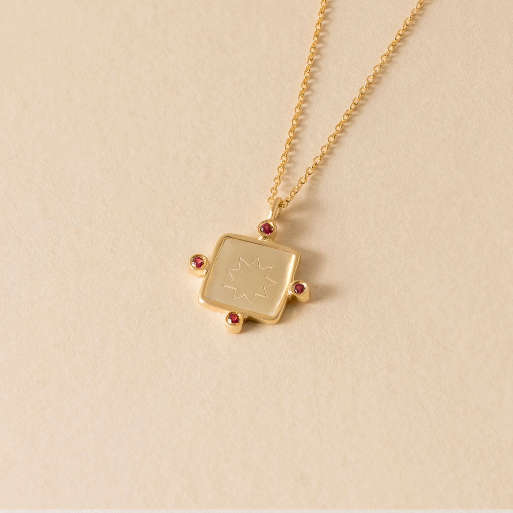 Gold necklace with a square nine pointed star pendant on a beige background