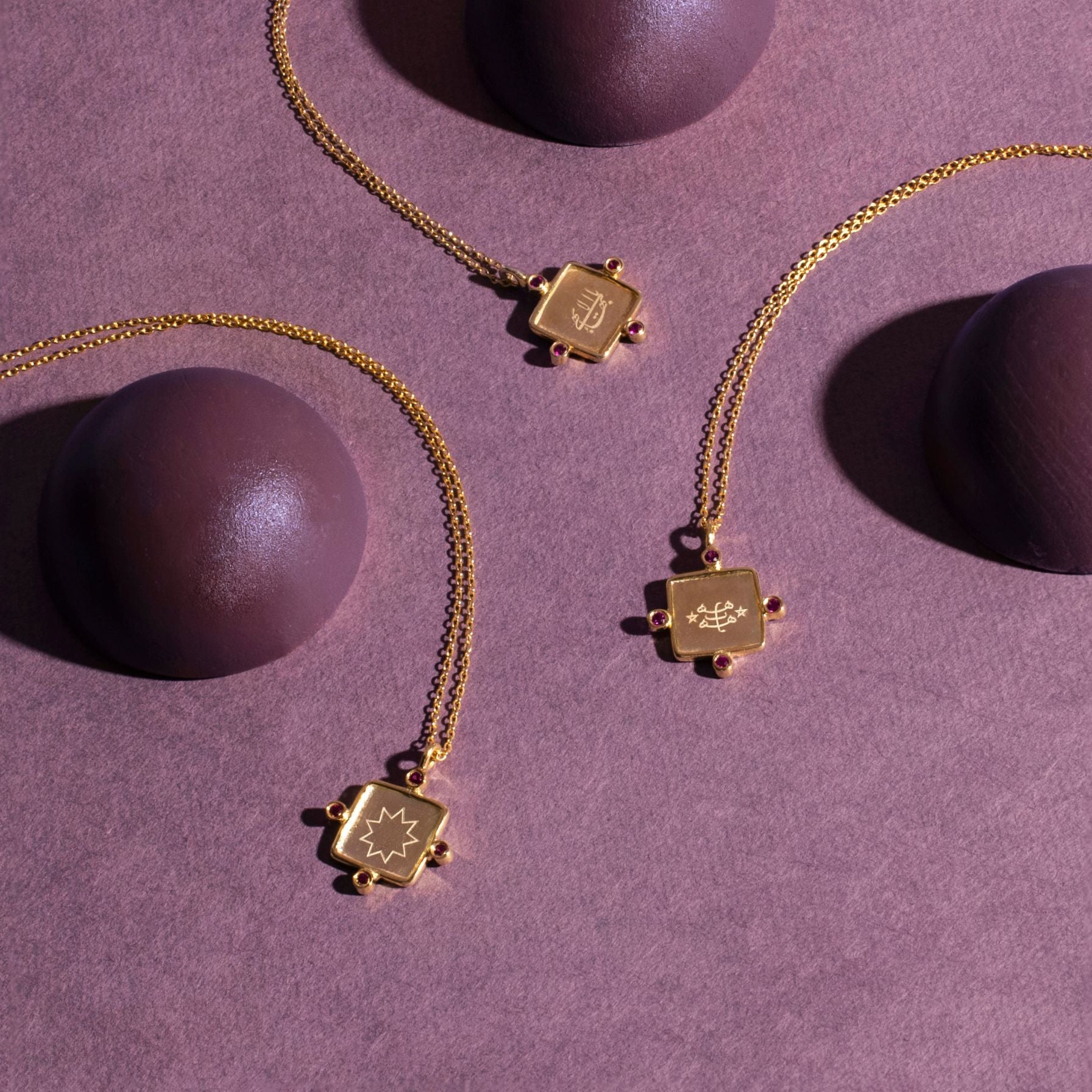 Gold bahai necklaces with square pendants on a purple surface