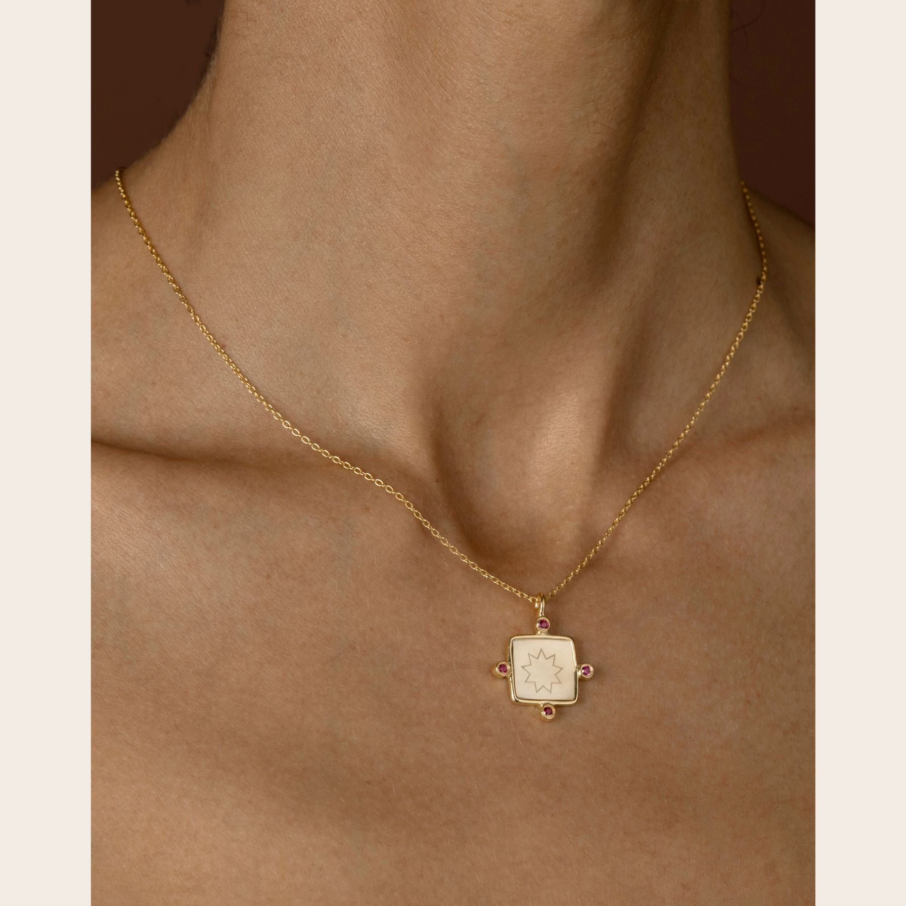 Gold necklace with a square nine pointed star pendant on a person's neck