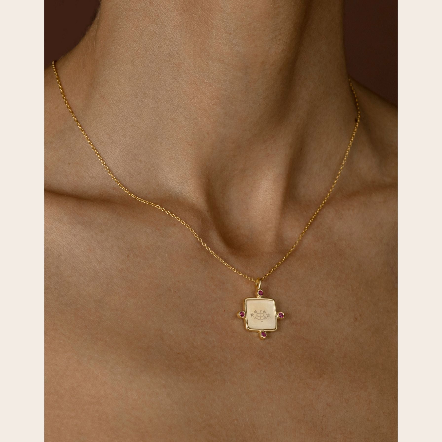Gold ringstone symbol necklace with a square pendant on a person's neck against a neutral background