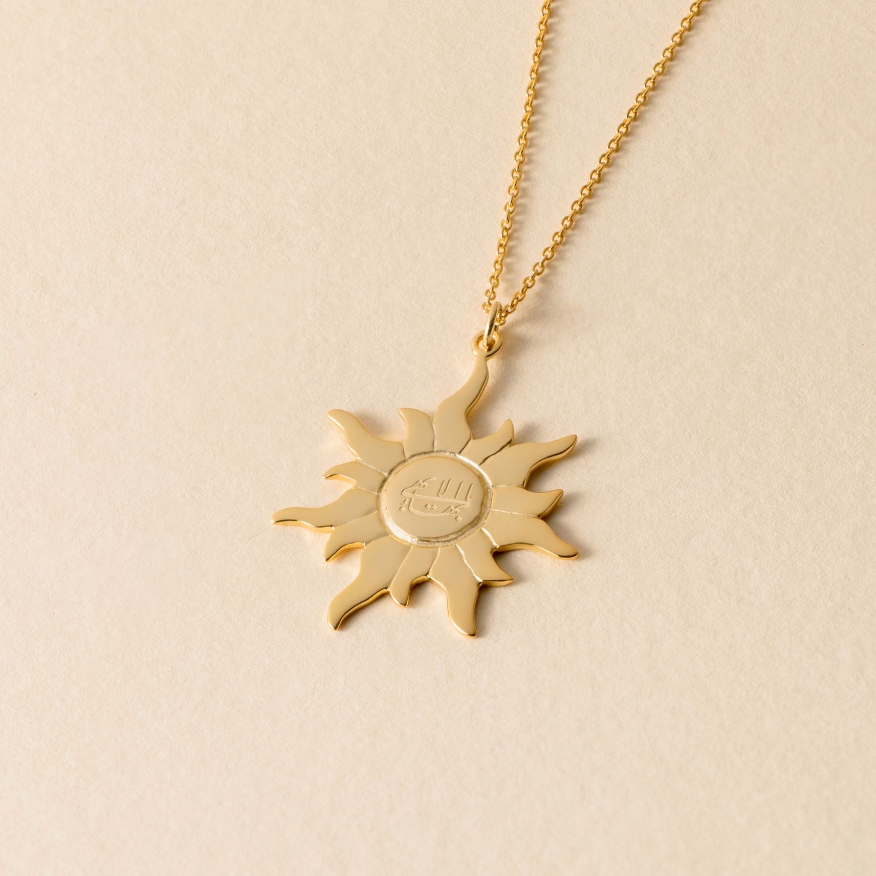 Gold sun-shaped greatest name pendant necklace on a beige background