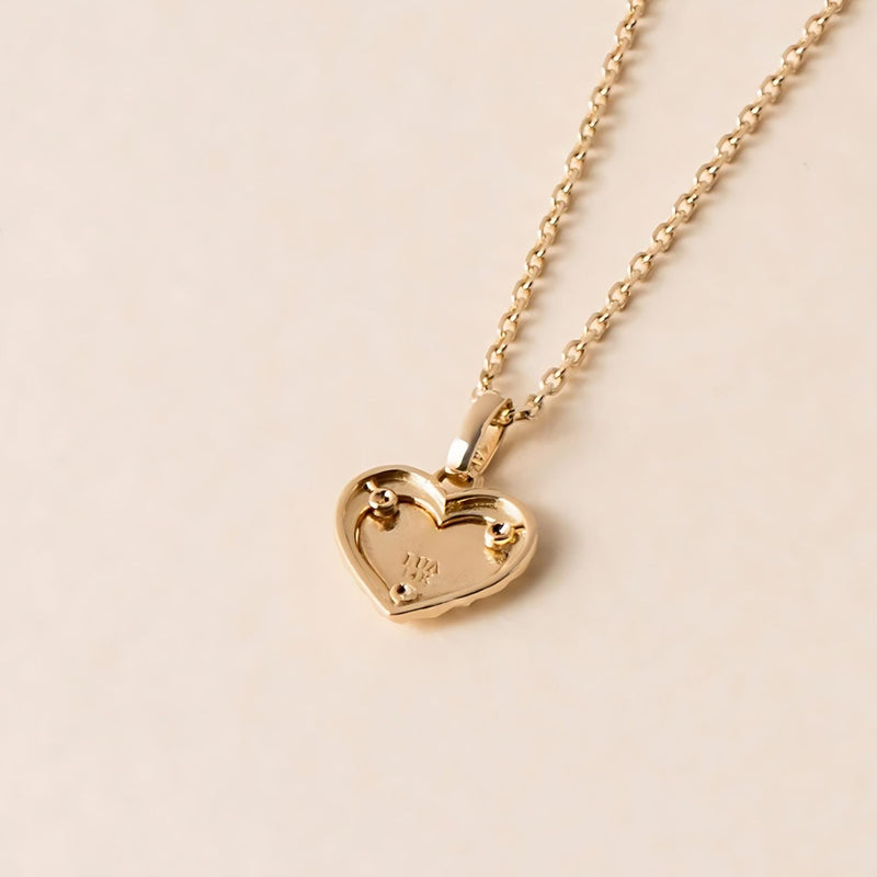 back of a gold love heart shaped pendant necklace placed on a light coloured background