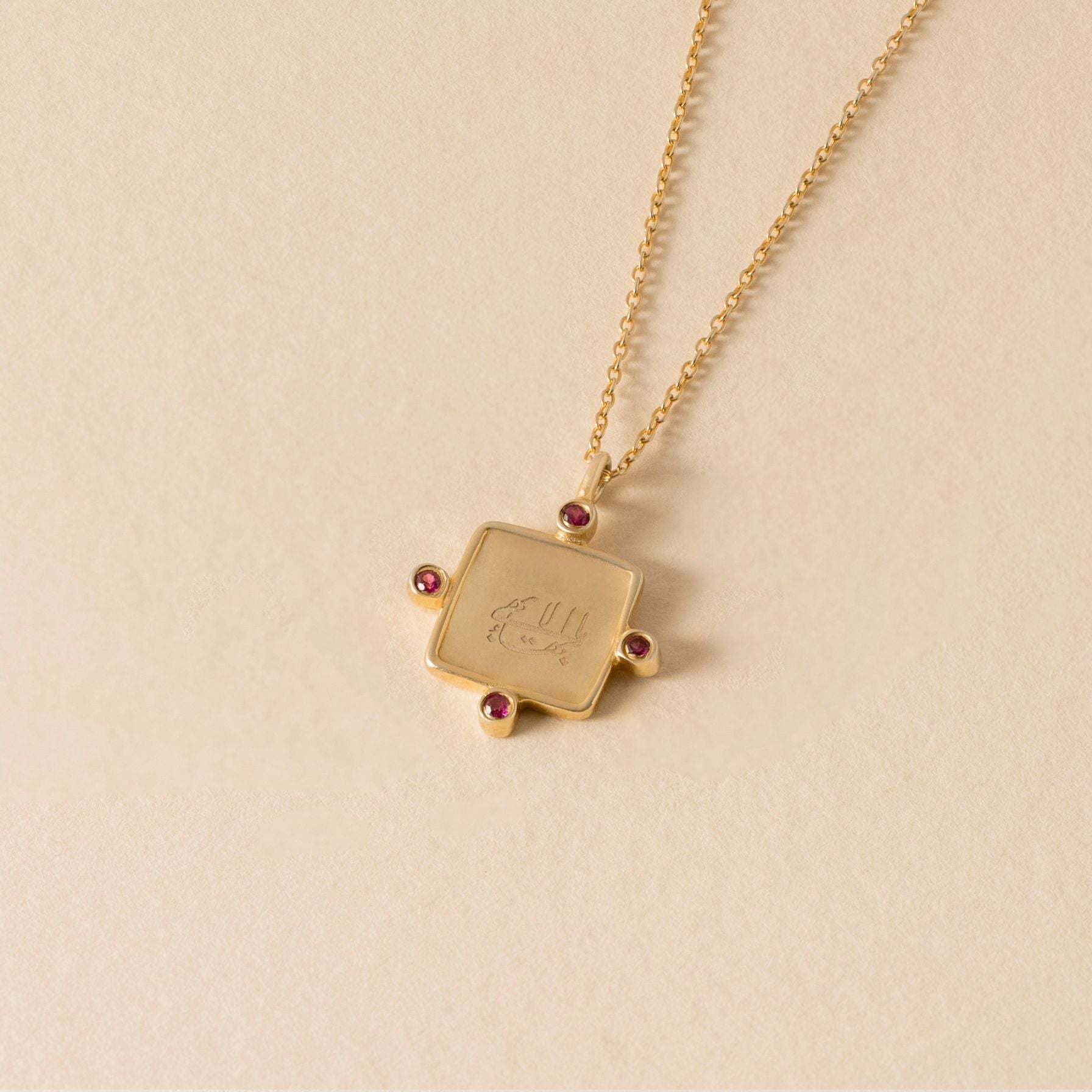 Gold necklace with a square greatest name pendant on a beige background