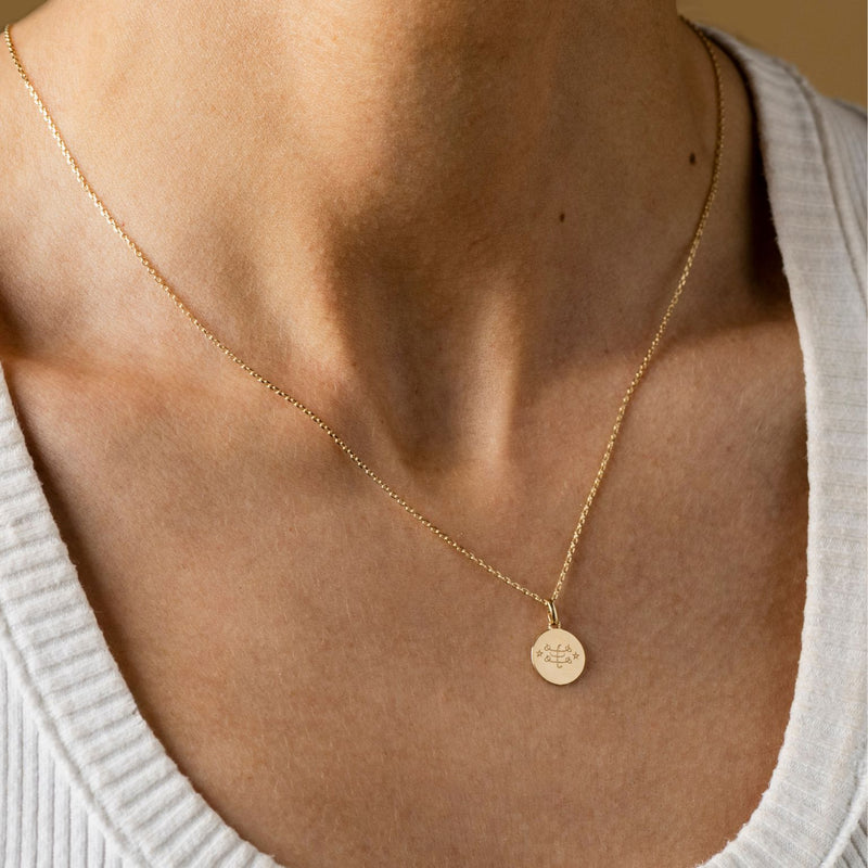 A close-up of a person wearing a Ringstone Symbol  Necklace, showcasing a gold chain with a circular gold pendant over a white ribbed shirt.