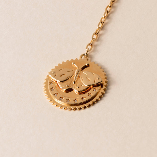 A close-up of a Butterfly Necklace featuring a gold pendant with a butterfly design and a row of stars etched below it, symbolizing transformation and resilience, attached to a gold chain.