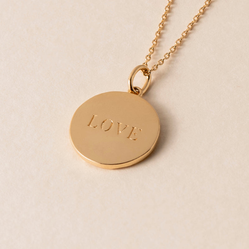 A stunning Love Heart Necklace, featuring a gold pendant inscribed with the word "LOVE," is displayed on a light background. This elegant piece, adorned with the symbol of love, serves as a timeless reminder of affection and devotion.