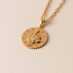 A gold pendant necklace with a circular medallion featuring an embossed design of a peacock and stars, capturing beauty through sensory experiences.