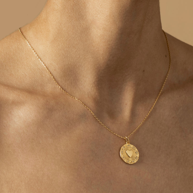 A close-up of a person wearing a radiant Love Heart Necklace with a round pendant featuring an engraved heart motif, symbolizing pure love.