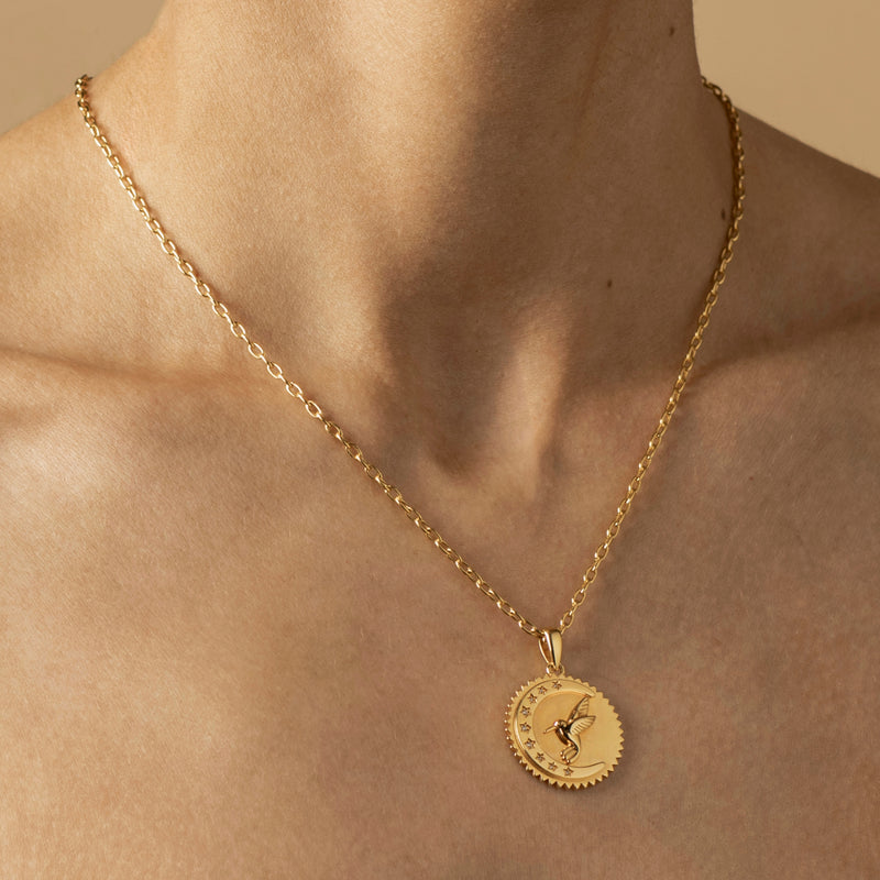 Close-up of a person's neck wearing a gold chain necklace with a round pendant featuring an engraved design, symbolizing life's blessings.