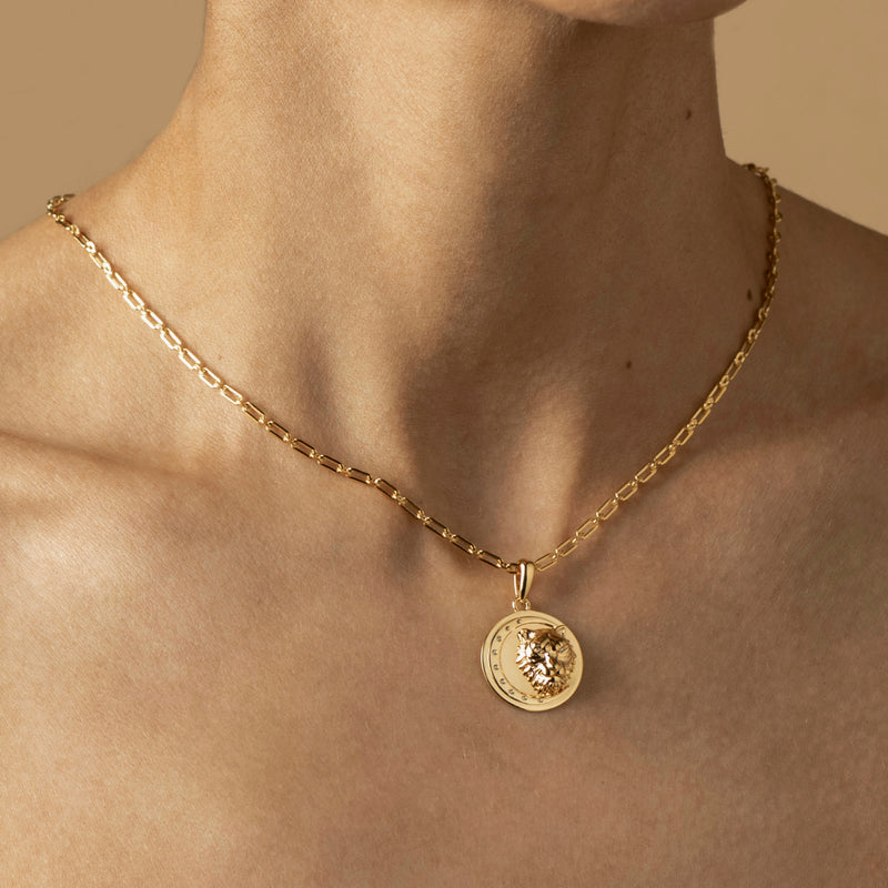 A person is wearing a gold chain necklace in 18k Gold Vermeil, adorned with a round pendant featuring a detailed lion head.