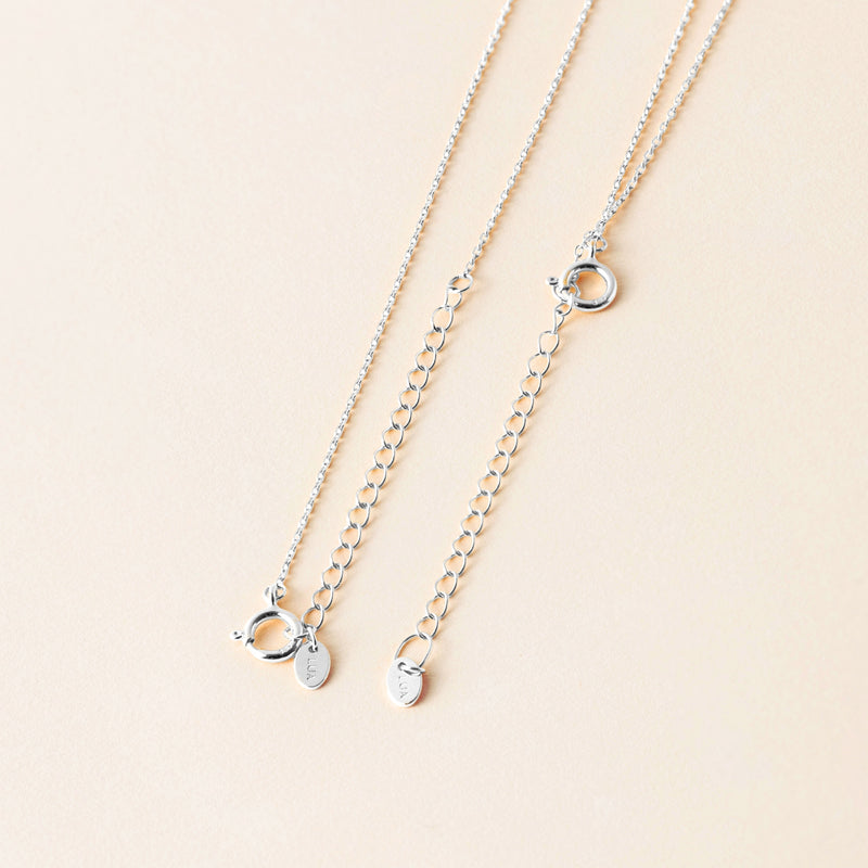 Two silver chains with delicate extension chains for adjustable length laid on a light beige surface, each featuring small circular clasps.