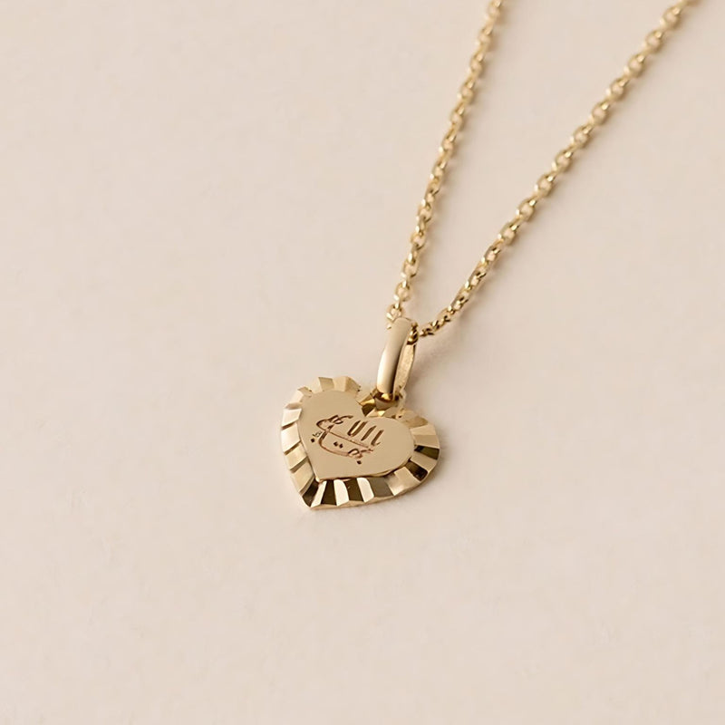 The Golden Love Heart necklace features a gold heart-shaped pendant with a decorative edge, hanging from a gold chain. It showcases engraved Greatest Name, complemented by radiant engraved sunrays.