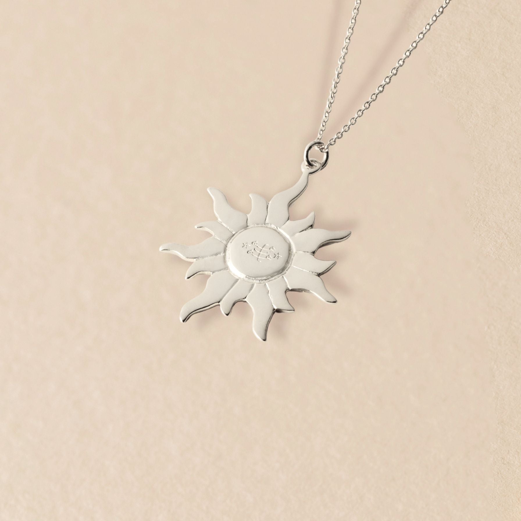Silver sun-shaped pendant necklace on a beige background