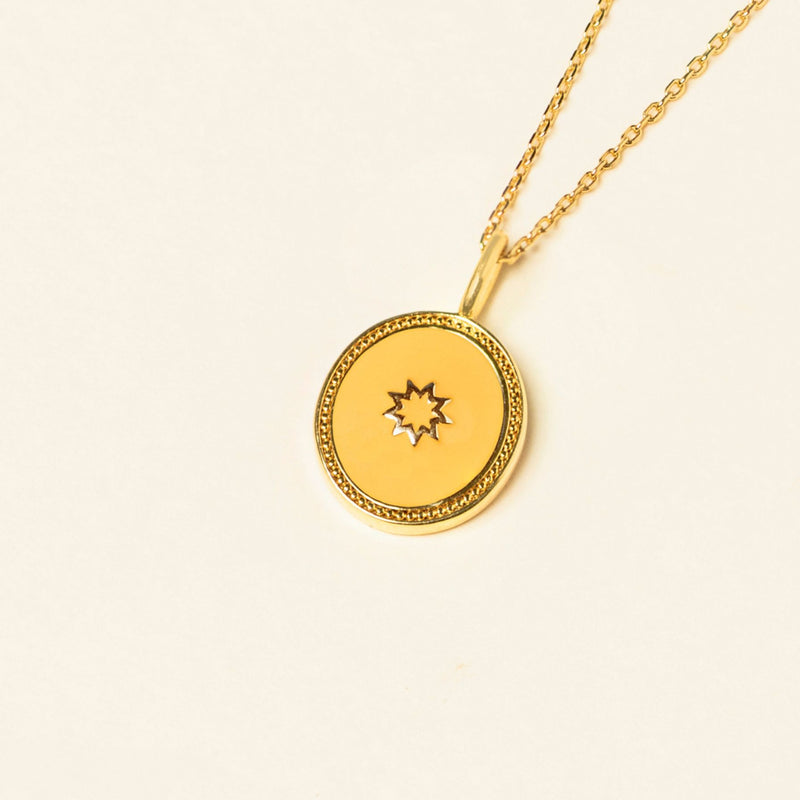 Gold pendant necklace with a circular medallion featuring the nine pointed star Symbol on an off-white background.