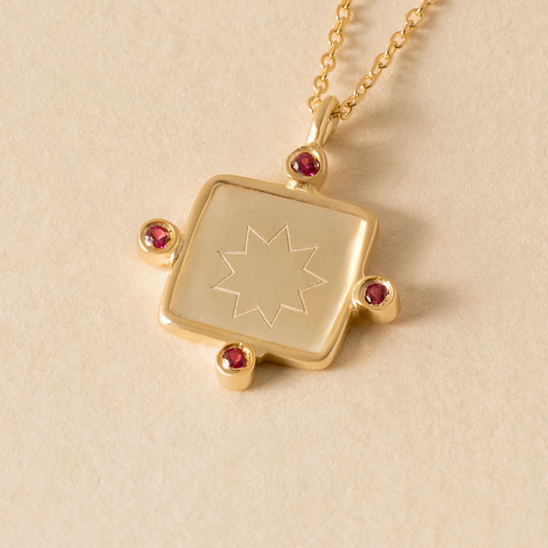 Gold necklace with a nine pointed star square pendant featuring a star design on a beige background