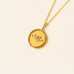 Gold pendant necklace with the Ringstone Symbol displayed on a plain beige background.