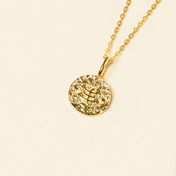 Gold pendant necklace with the ringstone symbol on a plain background.