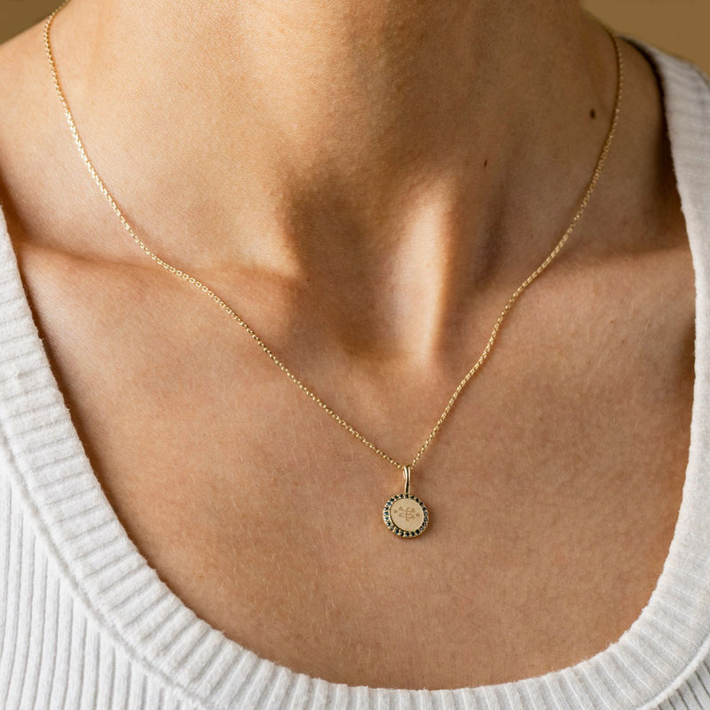 A person wearing a gold necklace with a round pendant featuring an engraved Ringstone symbol, encircled by blue diamonds