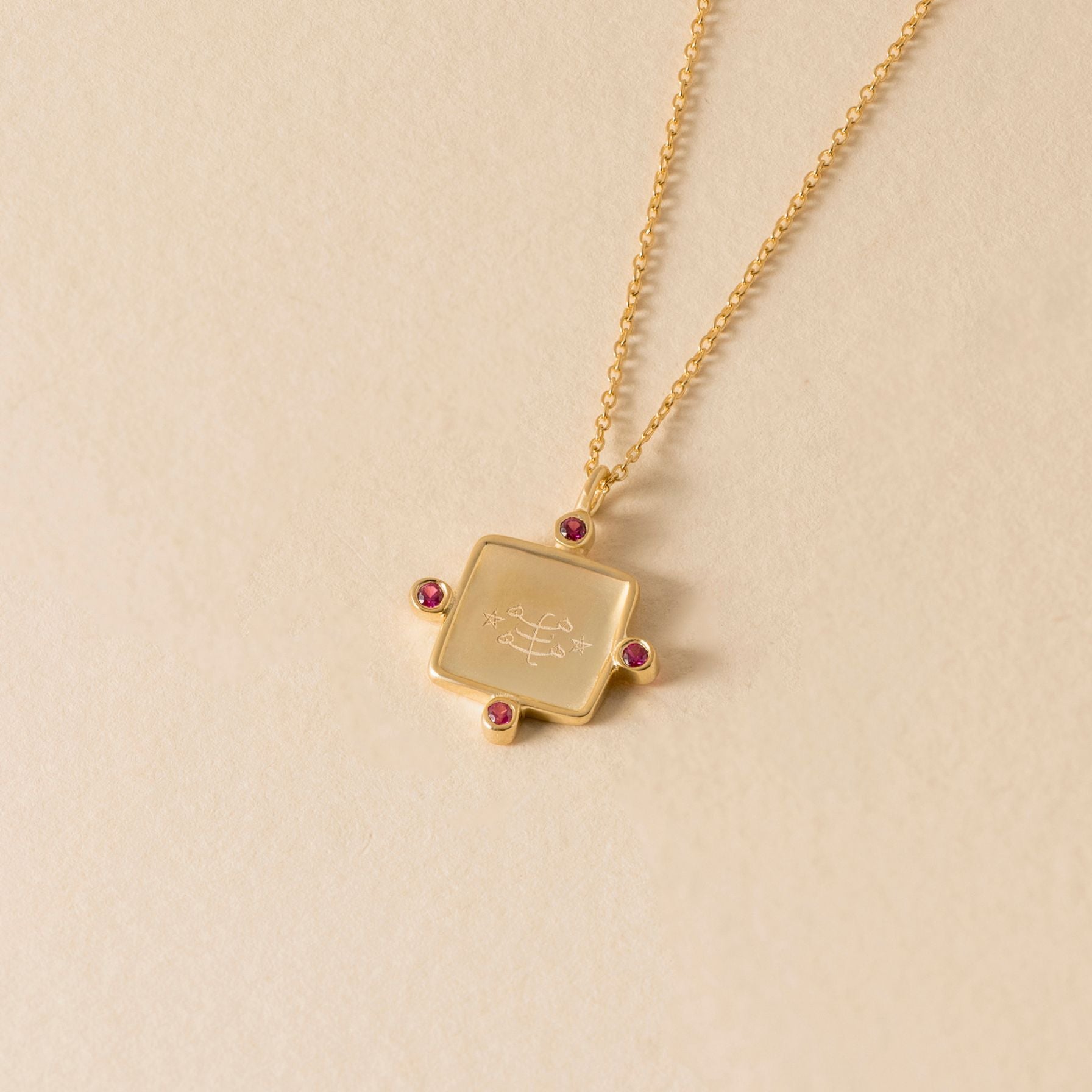 Gold ringstone symbol necklace with a square pendant on a beige background