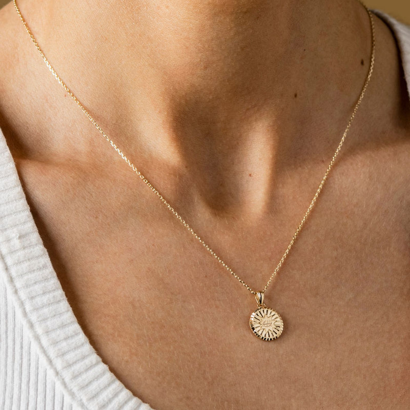 a persone wearing a round pendant necklace on a gold chain with the greatest name symbol engraved on it.